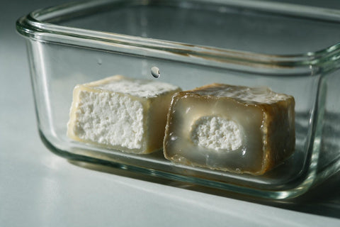 Zwei Stücke Graukäse in einer Glasdose im Vergleich: links ein junger mit krümeligem weißem Kern und schmalem Rand, rechts ein weiter gereifter mit breitem glasigem Rand und nur noch kleinem hellem Kern